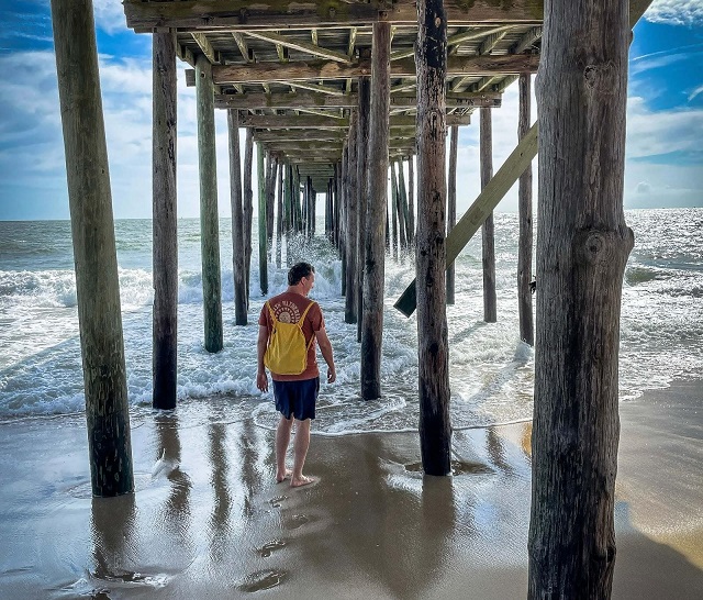 Man standing underneath a pier at the beach