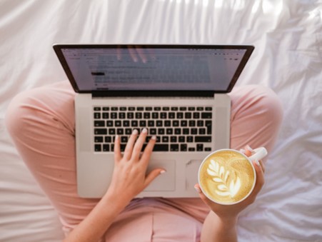 A picture of a someone holding a laptop on their lap and holding a cup of coffee