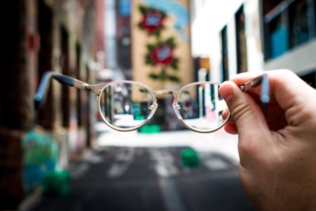 blurred image with glasses held by hand showing clear vision through their lenses.