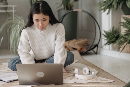 Woman Wearing White Sweater Sitting On Floor And Looking At Laptop