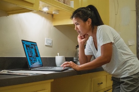 Woman Leaning On Kitchen Counter Using Laptop