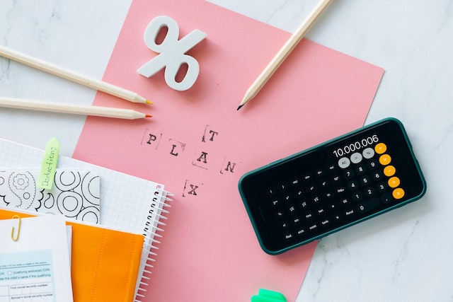 Pink paper on top of table surrounded by color pencils, cellphone, and notebook