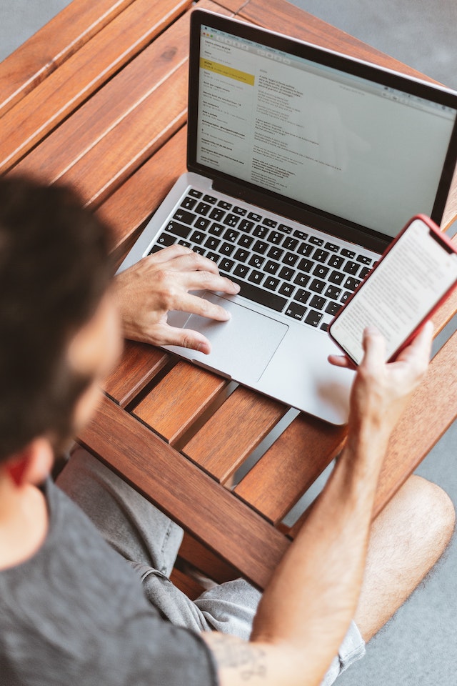 Man Sitting Down Holding A Cellphone And Laptop