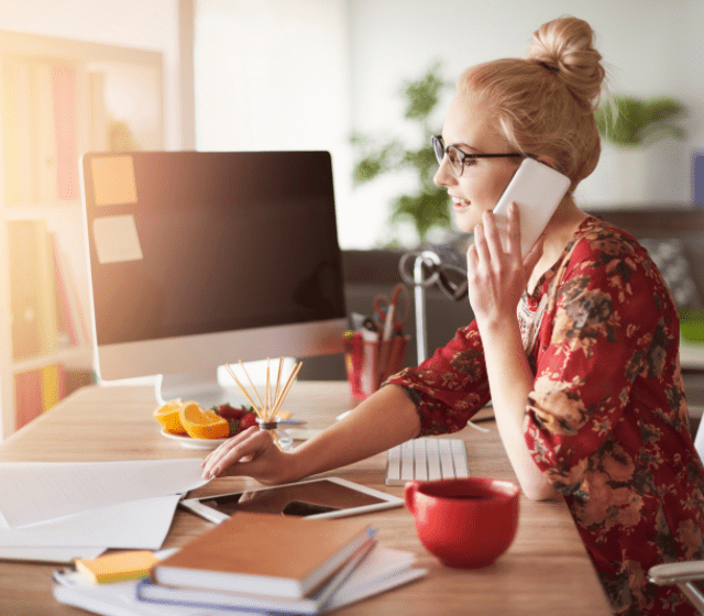 Woman Sitting On Desk Computer Talking On The Phone