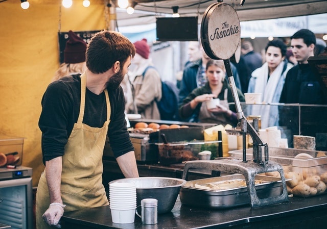 Cafe worker looking over his shoulder at a line of customers.