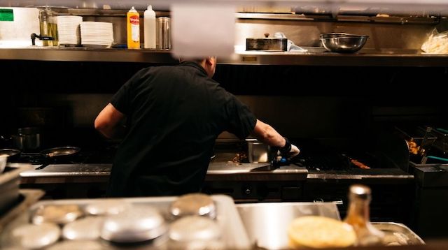 Man Working at a Grill with His Back to the Camera