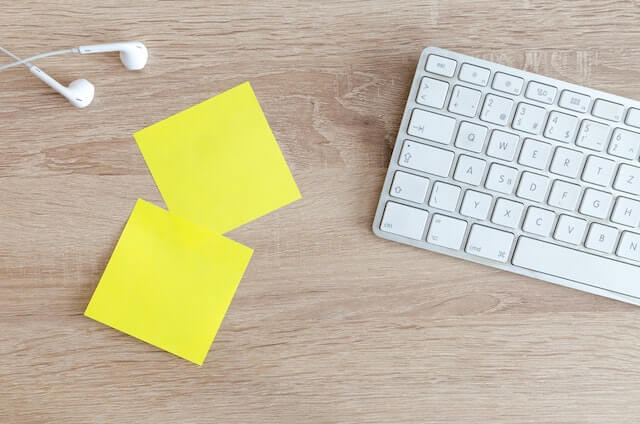 Yellow sticky notes on desk with keyboard and earphones nearby