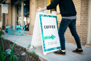 Man placing sign on sidewalk advertising a coffee shop