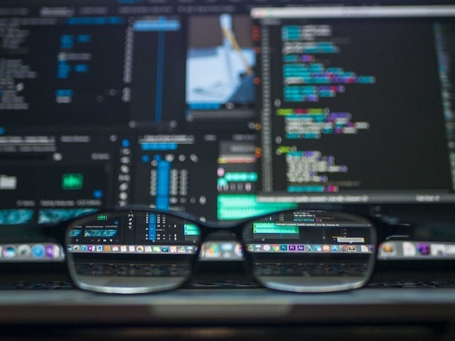 Closeup of eyeglasses on desk with computers and screen in background