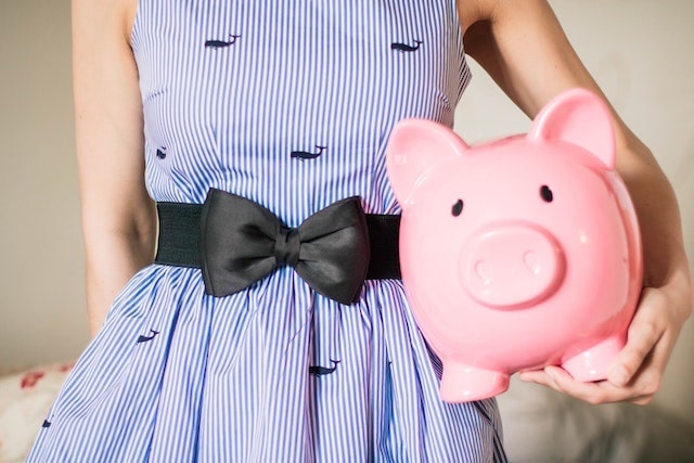 Close-up of woman in blue dress holding a pink piggy bank