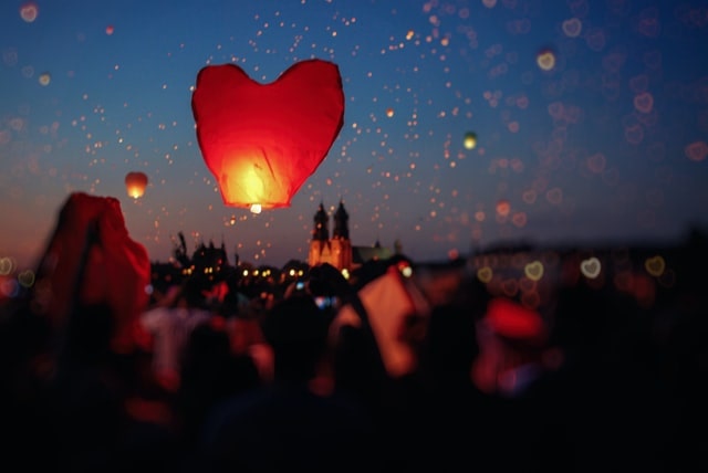 Crowd of people launching heart-shaped lanterns at dusk