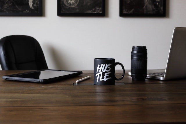 Desk with coffee mug that reads”hustle” on it