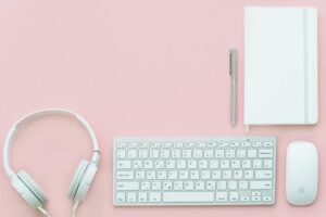 Headphones keyboard mouse and planner on pink desk