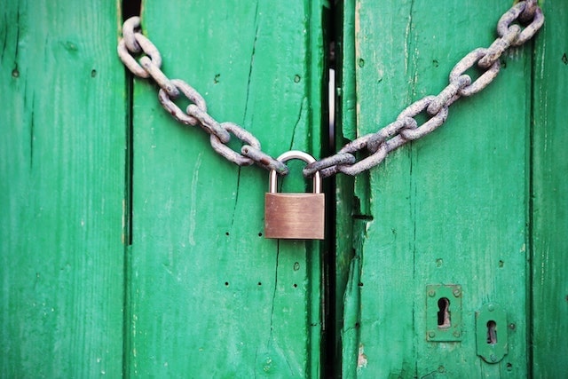 Locked padlock hanging from a chain on green door