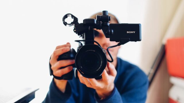 Man in a blue jumper holding a video camera