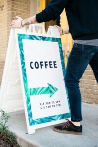 Man Placing Open Sign Outside a Coffee Shop