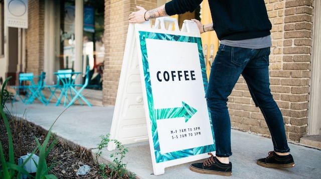 Man setting up coffee shop sign on sidewalk