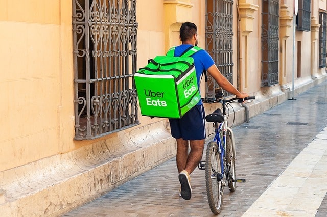 Man with an Uber Eats backpack walking a bike