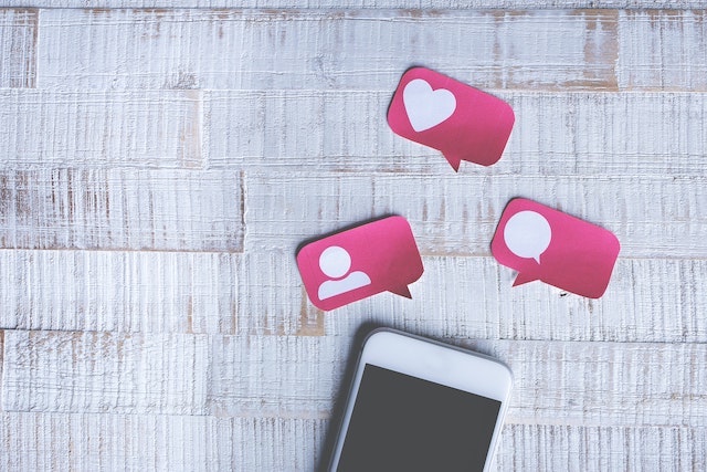 Mobile phone on table with paper cutouts symbolizing social media interactions