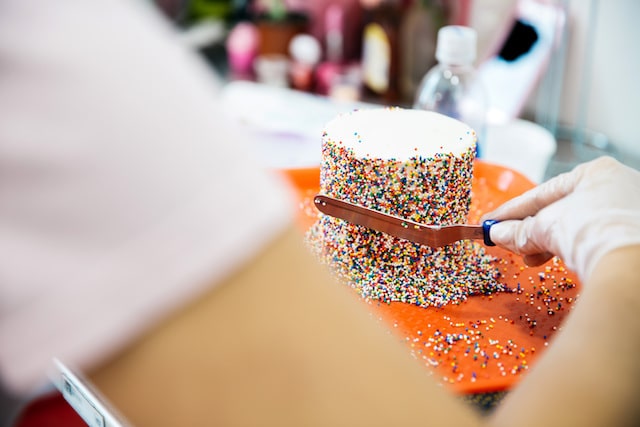 Person decorating a cake with colorful sprinkles