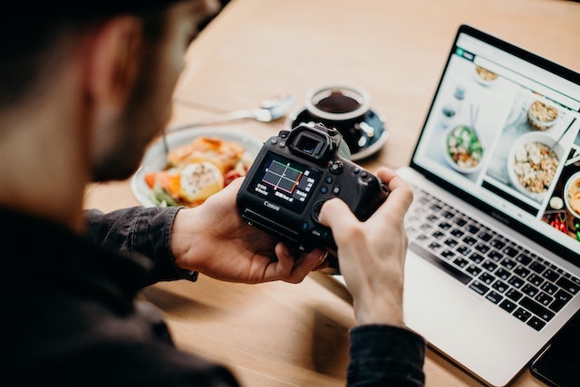 Person looking at DSLR camera with open laptop nearby