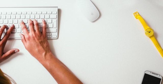 Person typing on a computer keyboard on a white desk