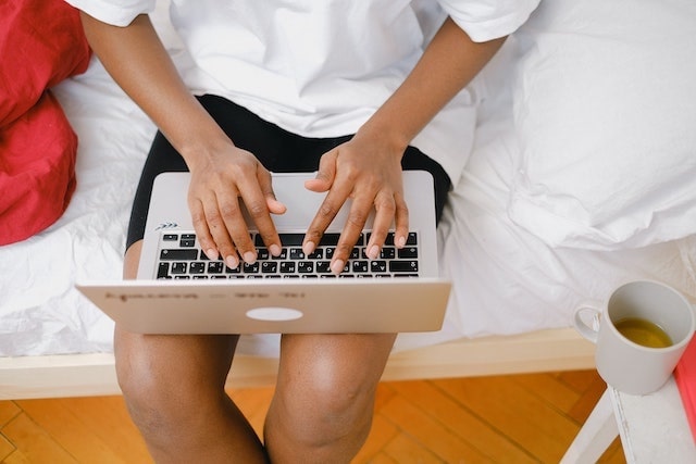 Person typing on laptop while sitting in bed