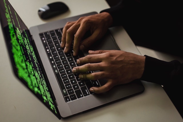 Person typing on laptop with green code on the screen