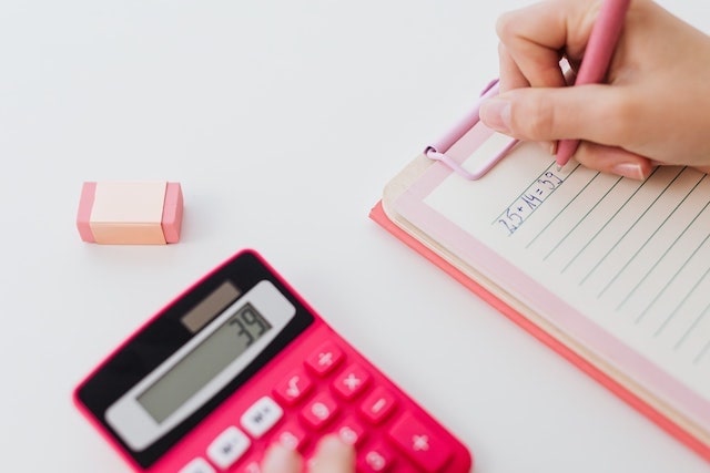 Pink calculator next to person writing numbers on notepad