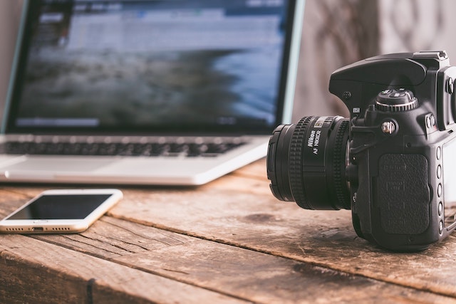 Professional camera sitting next to smartphone and laptop on desk