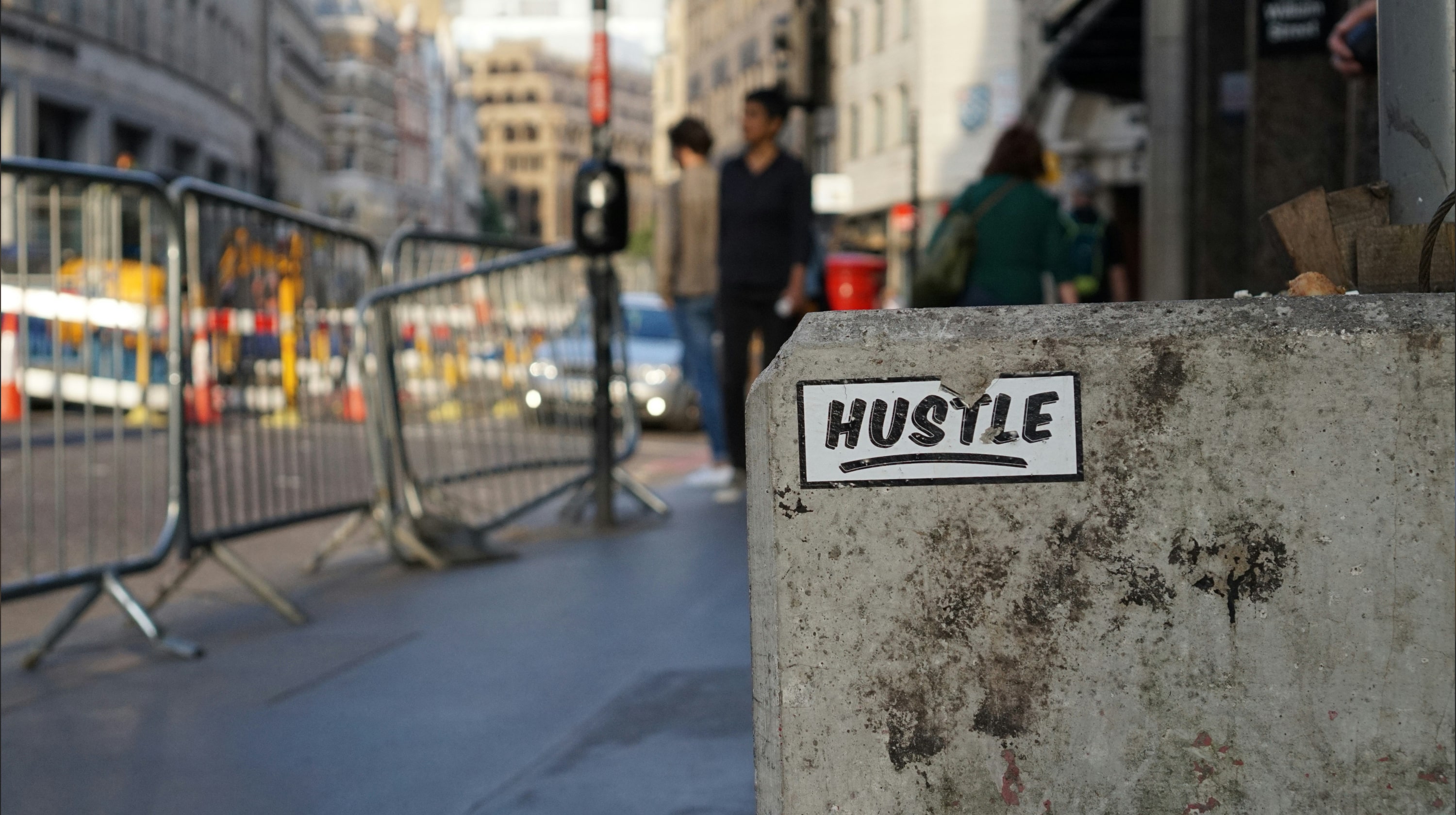 City street scene with a sticker that says hustle pasted to a wall