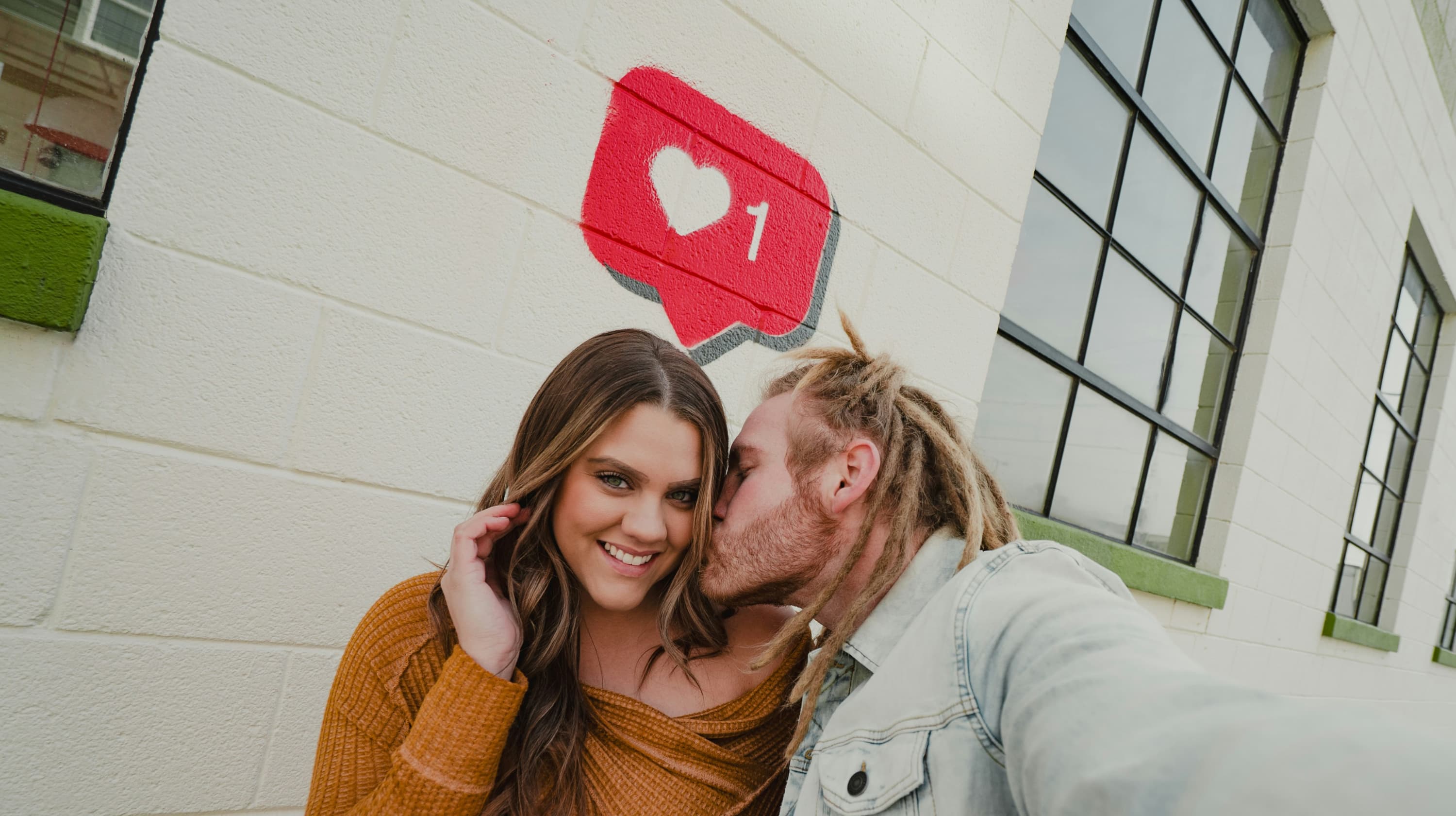 Man kissing a woman under a social icon painted on a wall