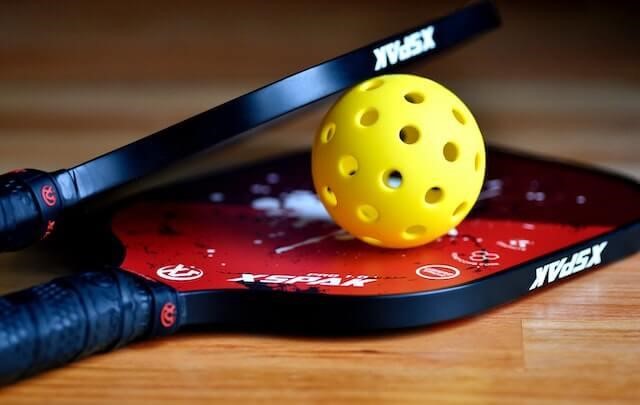 Pickleball resting between two black paddles