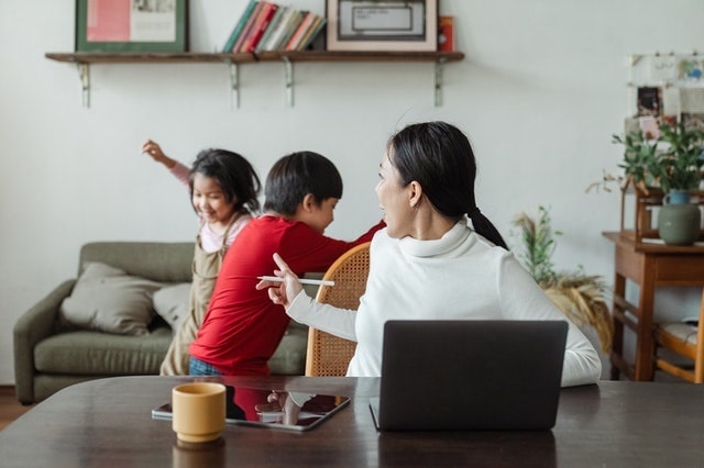 Woman with laptop talking to children behind her