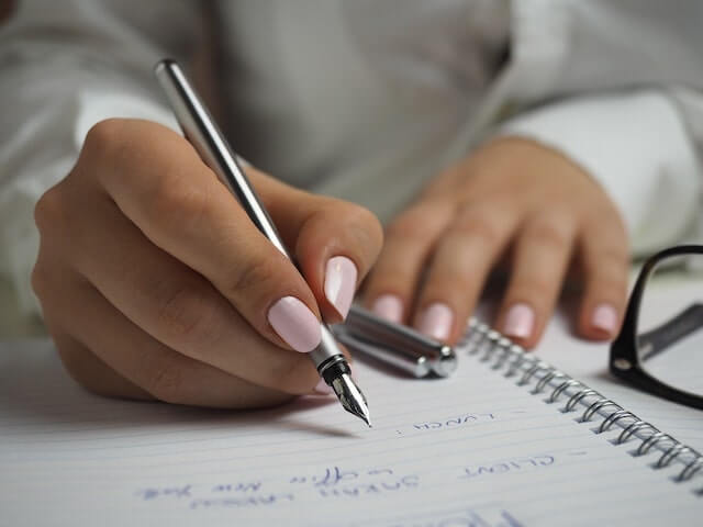 Woman writing in a notebook with a silver pen