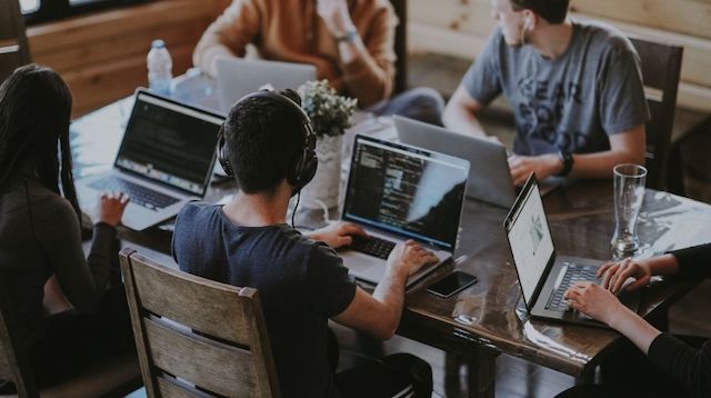 Group of people sitting around a table working on laptops