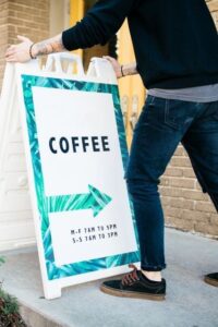 Man Positioning a Free Ad Sign Outside a Coffee Shop