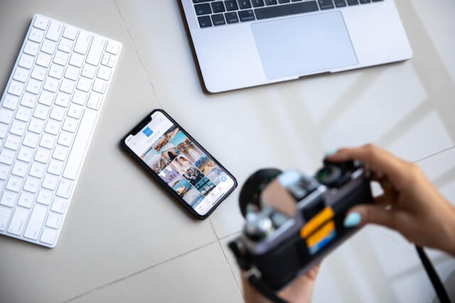 Person holding camera with smartphone and laptop nearby