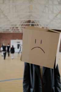 Person seperated from group wearing a cardboard sad face over their head