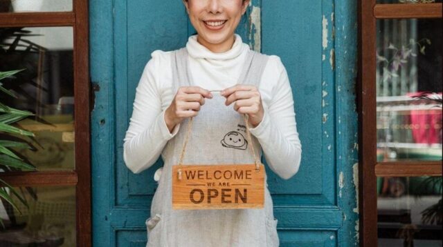 Shop Owner Standing in Front of Blue Door with Open Sign