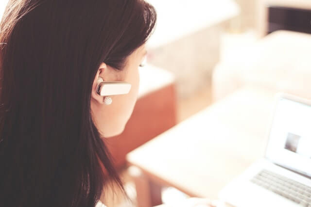 Woman with bluetooth earpiece working on laptop.