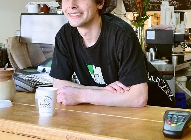 Young coffeehouse worker smiling at counter