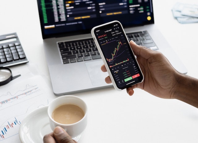 Person holding phone near computer with charts showing.