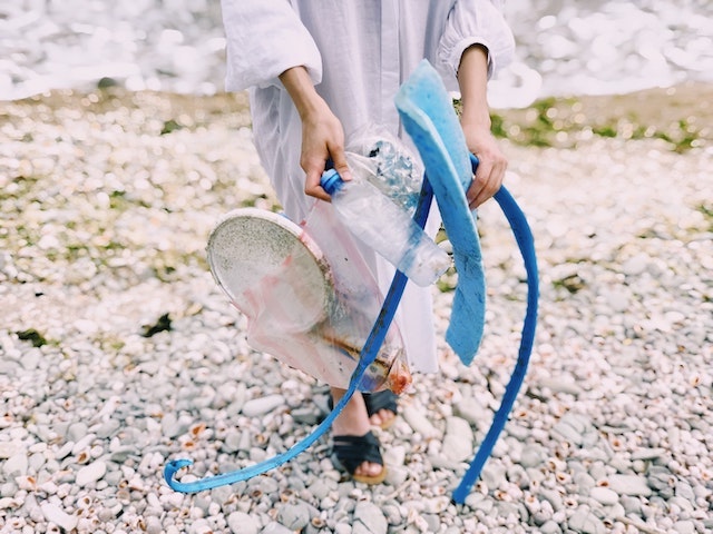 Person on a beach carrying plastic bottle and other trash