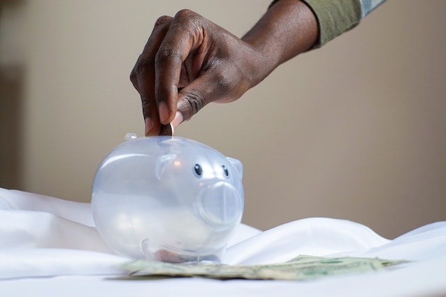 Close up of person placing coin in clear piggy bank