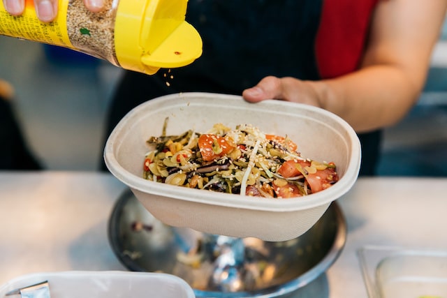 Person seasoning food in cardboard takeout tray