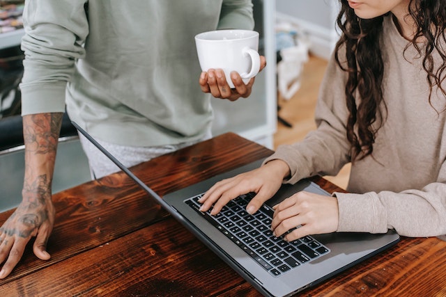 Person working on laptop with another person standing nearby