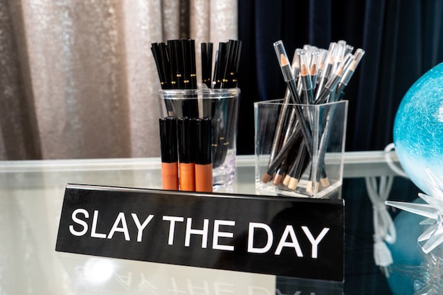 Sign reading “Slay the Day” with beauty products in background