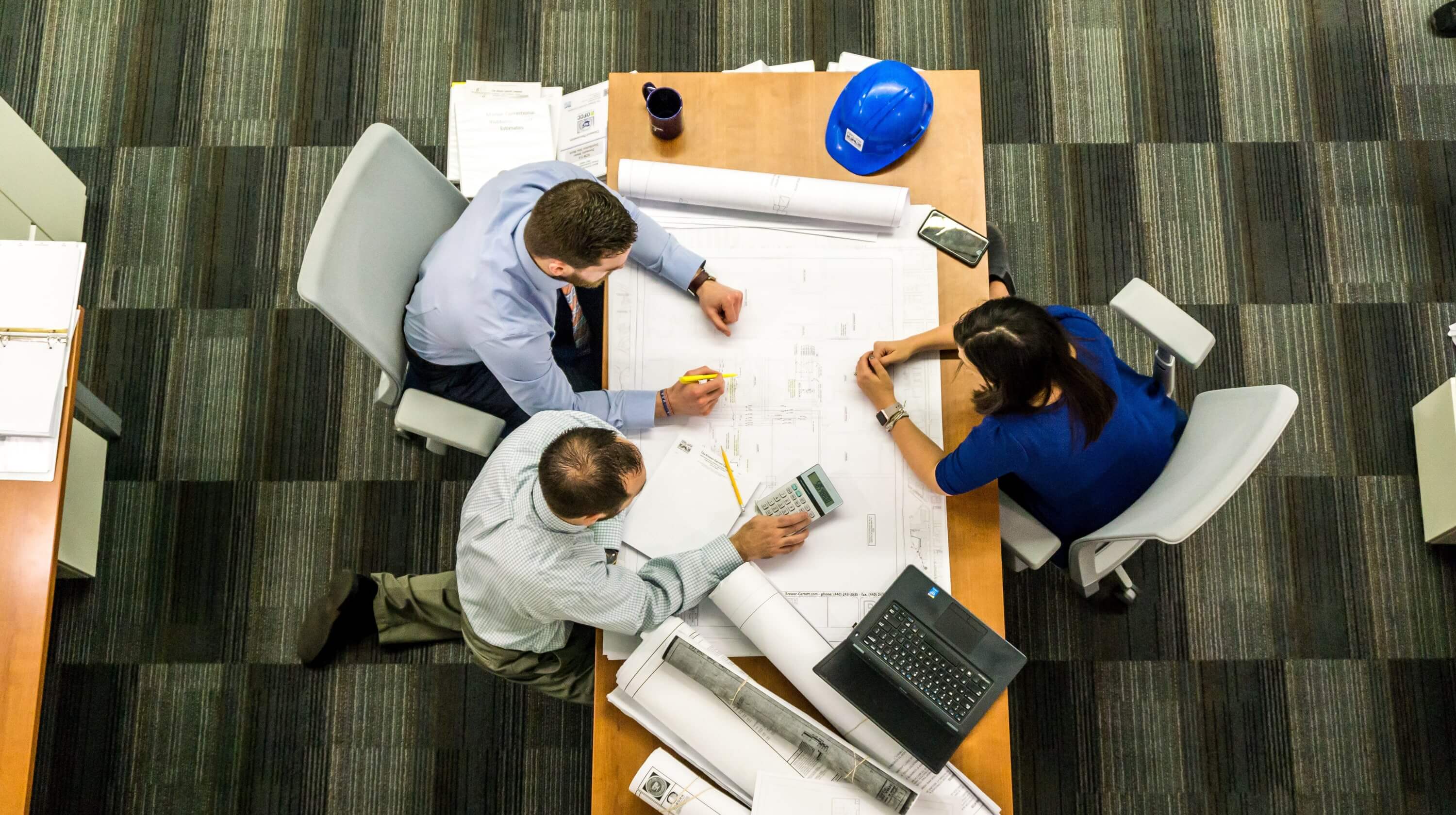 Overhead view of three people at a desk looking at plans