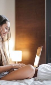 Woman sitting on bed looking at laptop and smiling